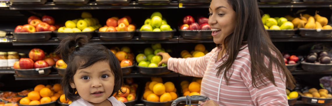 A woman and young girl shop for fruit in a grocery store.