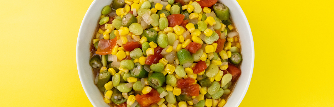 A bowl of Corn, Lima Beans, Okra, and Tomatoes on a yellow background