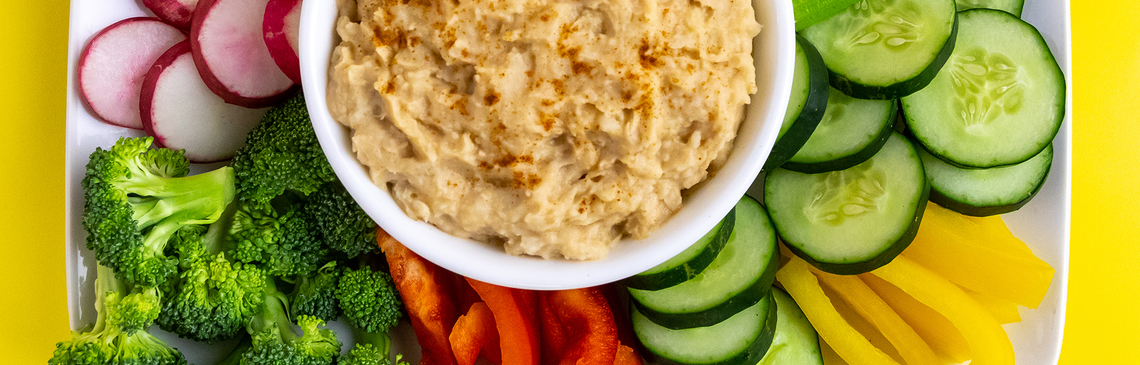 Bowl of hummus on tray with spread of vegetables.