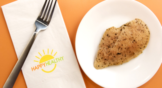 A grilled chicken breast on a plate with a fork and napkin beside.