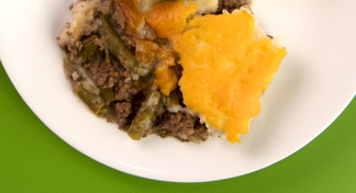 A white plate filled with Shepherd's Pie; a recipe using ground beef, green beans, mashed potatoes, and cheese.