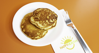 A white plate with two pancakes on an orange background, next to a napkin and fork
