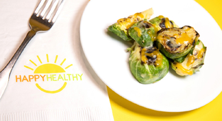 Baked Brussels Sprouts on white plate next to HappyHealthy napkin and fork
