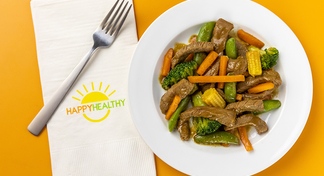 Beef Stir Fry in white bowl next to HappyHealthy napkin and fork