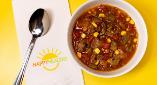 A white bowl filled with beef taco soup next to a spoon and HappyHealthy napkin