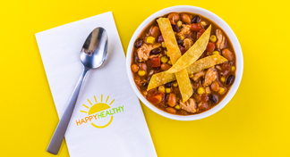 Bowl of Chicken Taco Soup with spoon on HappyHealthy napkin.