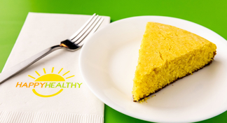 A white plate with a wedge of cornbread next to a fork and Happy Healthy napkin