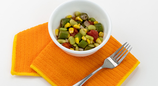 A bowl of Corn, Lima Beans, Okra, and Tomatoes next to an orange napkin