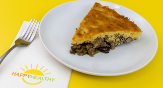A slice of cowboy casserole on a white plate next to a fork and HappyHealthy napkin