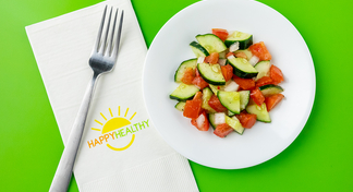 Cucumber and Tomato Salad on white plate next to HappyHealthy napkin and fork