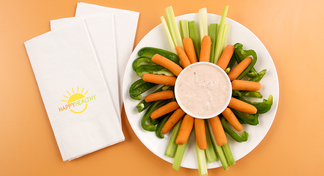 Plated fresh vegetables: baby carrots, celery, and bell peppers surrounding a bowl of sour cream and salsa dip.