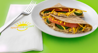 A white plate with a hummus and vegetable wrap next to a fork and Happy Healthy napkin
