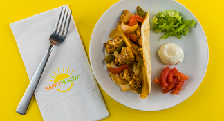 One Pan Fajitas on white plate with toppings and with a fork on a HappyHealthy napkin.