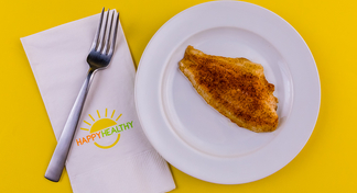 Fillet of Oven Blackened Catfish on white plate next to HappyHealthy napkin and fork