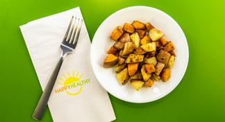 A plate of cubed and roasted potatoes with a HappyHealthy napkin and fork to the side.