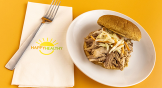 Slow Cooker Pulled Pork on a bun, plated on a white plate next to a HappyHealthy napkin and fork