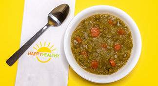 A bowl of split pea soup in a white bowl next to a HappyHealthy napkin and spoon