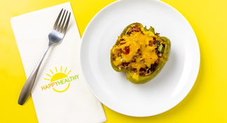 A stuffed bell pepper on a white plate next to a Happy Healthy Napkin and Fork