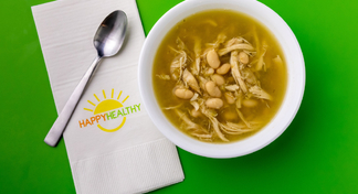 White chicken chili in white bowl next to HappyHealthy napkin and spoon.