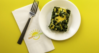 A serving of egg and spinach casserole on a white plate with a fork and napkin to the side.