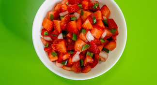A white bowl of strawberry salsa on a green background
